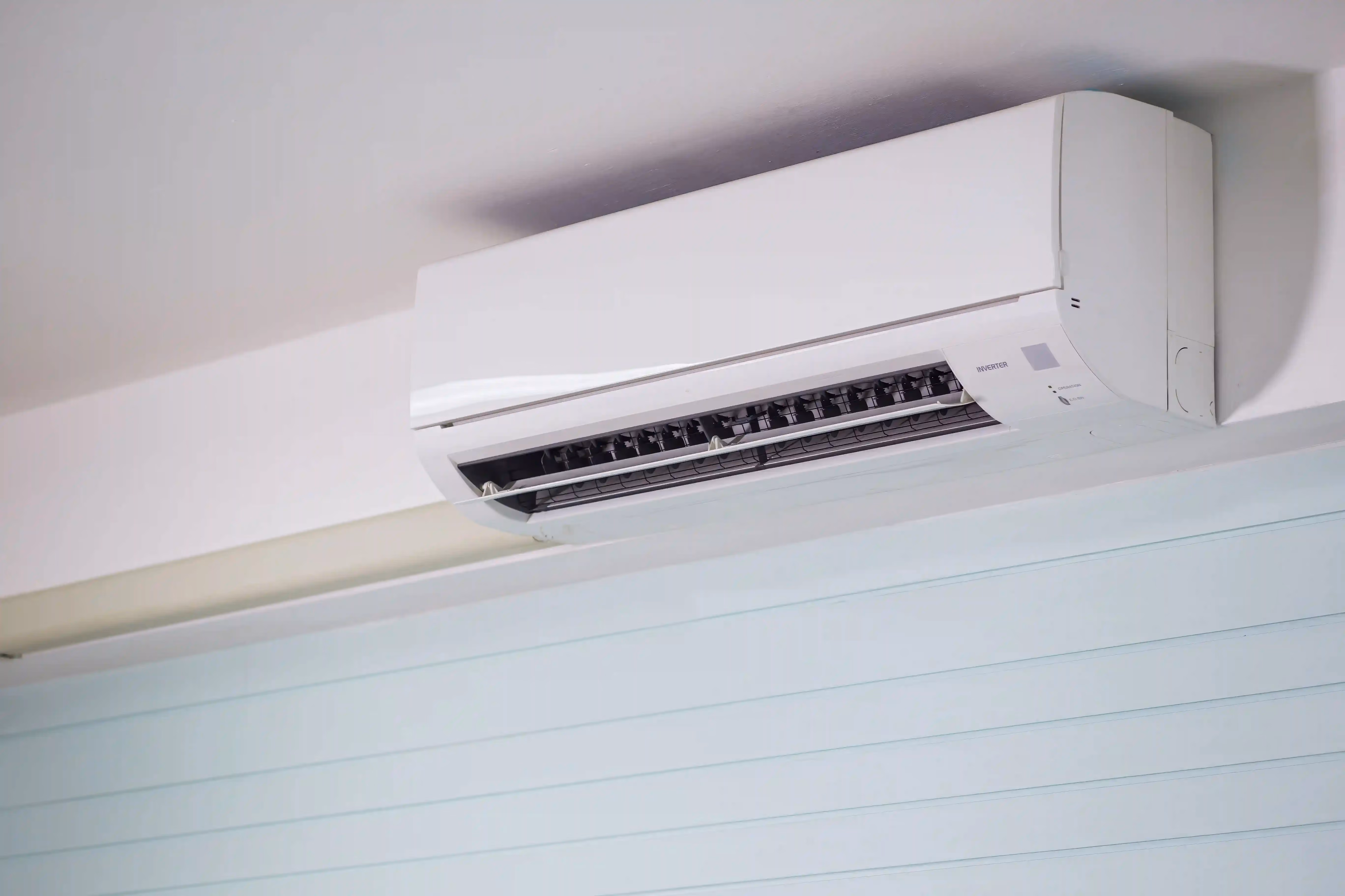 A new white split system indoor unit mounted high on a pale wall above white weatherboard-style panelling